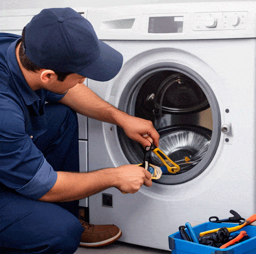 Técnico reparando una lavadora en casa con caja de herramientas al lado.